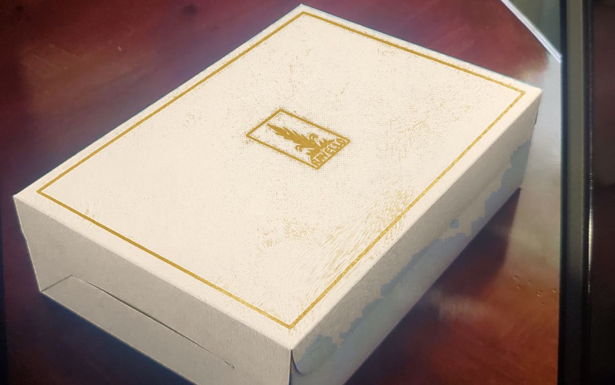 A cream gift box with a gold border and gold wheat mark on the lid, sitting on a dark wooden table